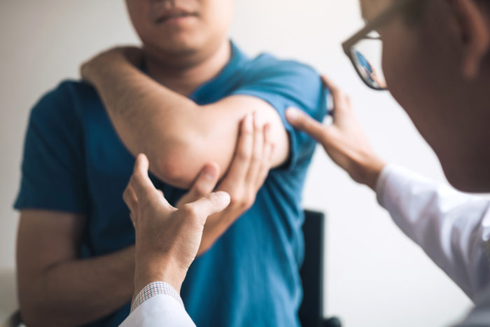 Physician examining an adult patient’s shoulder during an orthopedic consultation